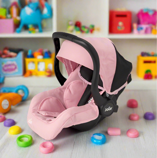 Joie I-Gemm Dolls Car Seat in pink and black, featuring a realistic design with secure harness, padded interior, and carry handle, perfect for children to safely transport their dolls during playtime
