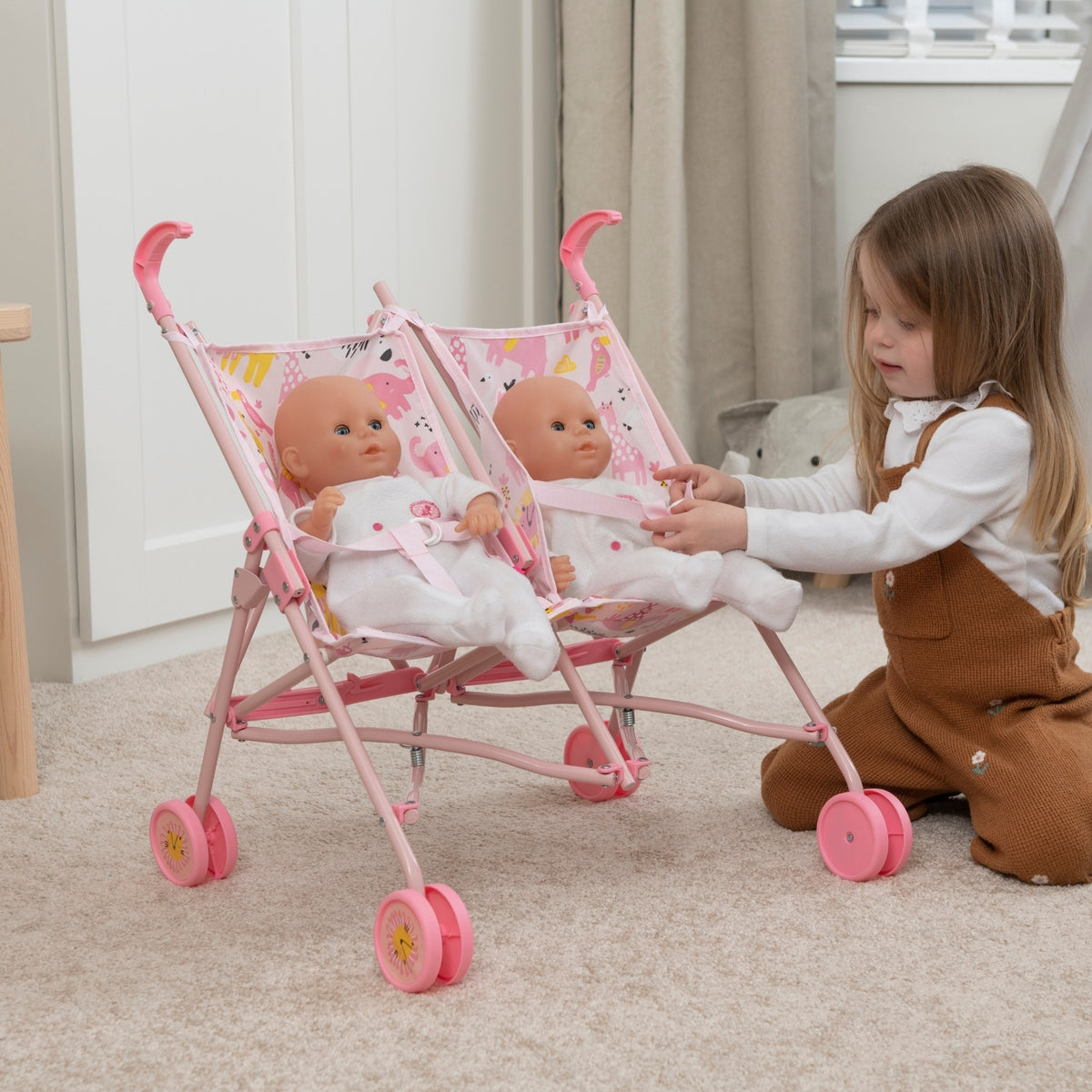 Child playing with a pink double stroller toy and dolls indoors.