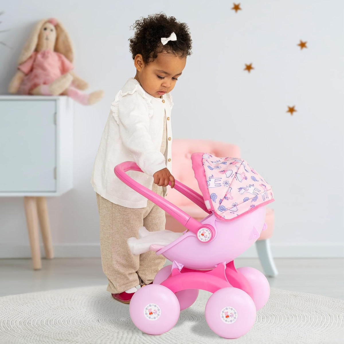 A child pushing the Peppa Pig 4-in-1 Pram with a doll inside, styled as a front-facing pushchair. The light pink body and Peppa Pig details enhance imaginative play.