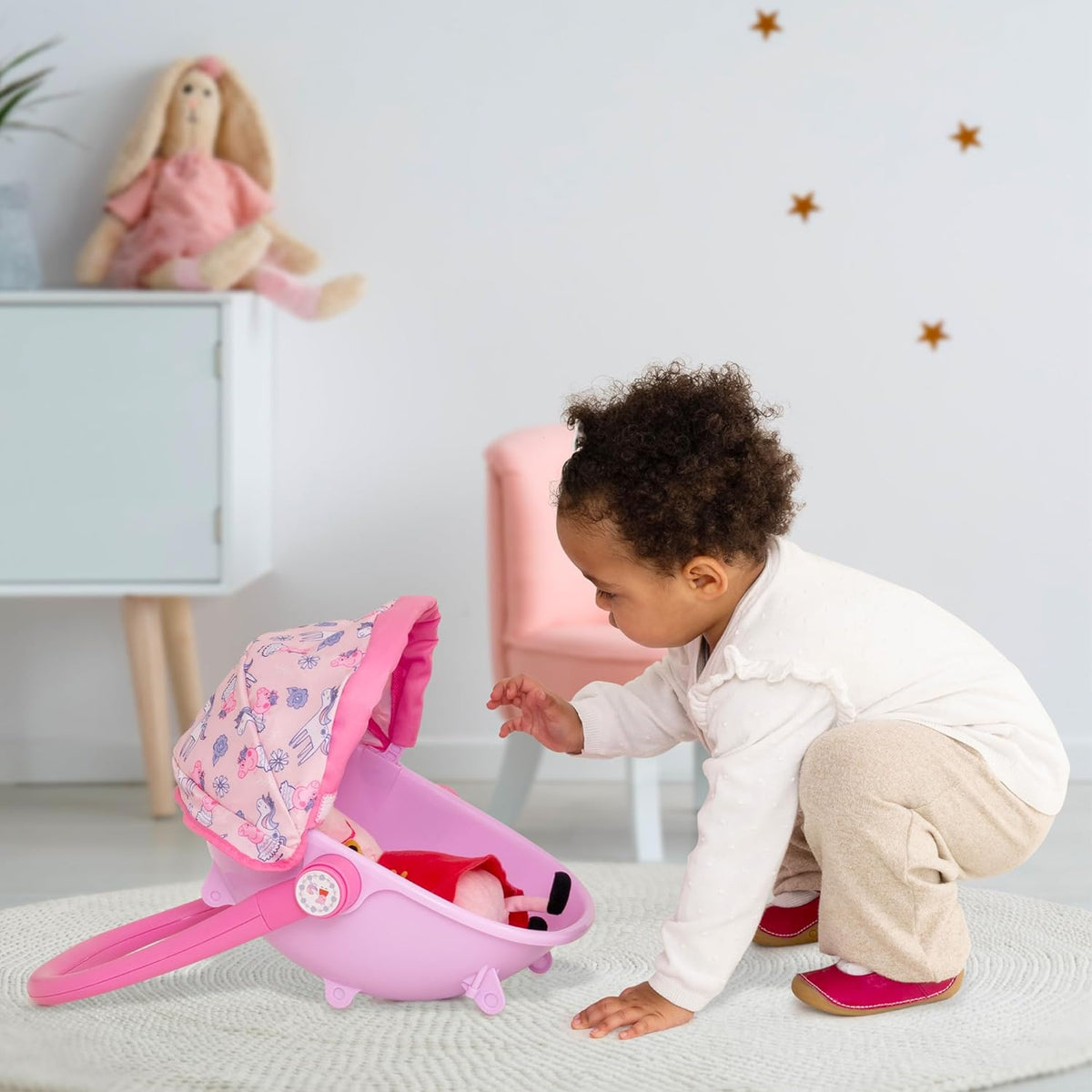 A child pushing the Peppa Pig 4-in-1 Pram with a doll inside, styled as a front-facing pushchair. The light pink body and Peppa Pig details enhance imaginative play.