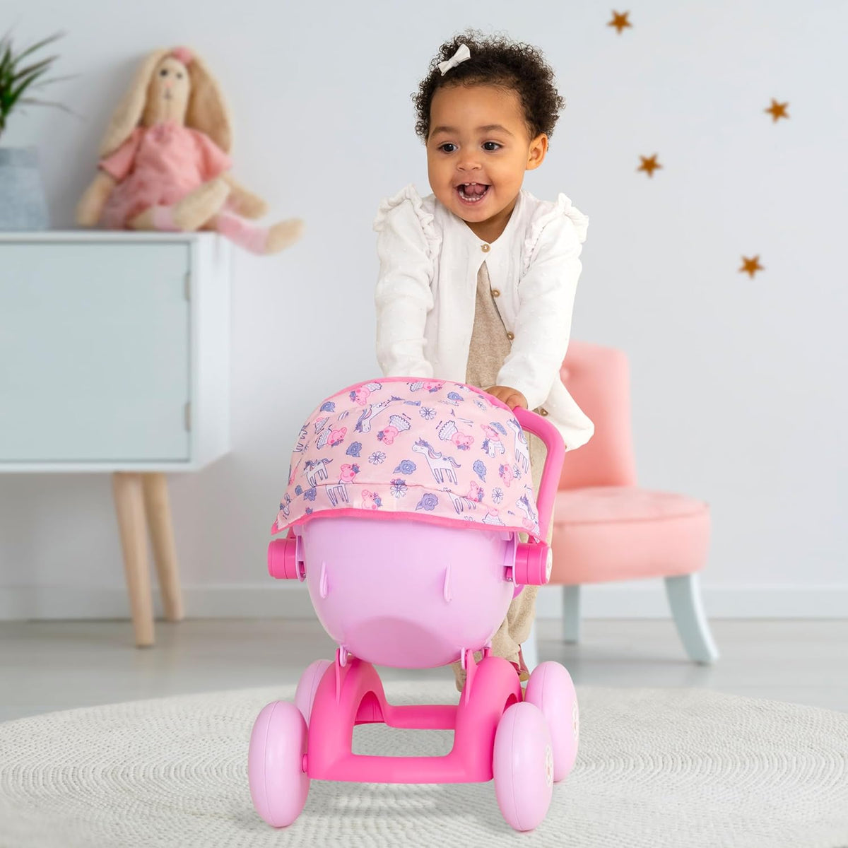 A child pushing the Peppa Pig 4-in-1 Pram with a doll inside, styled as a front-facing pushchair. The light pink body and Peppa Pig details enhance imaginative play.